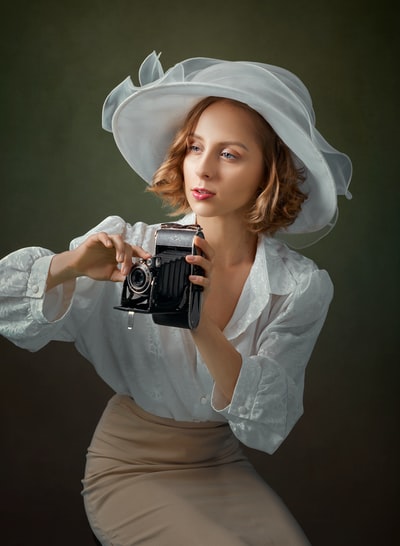 女人在白色的长袖衬衫黑色和银色的相机
